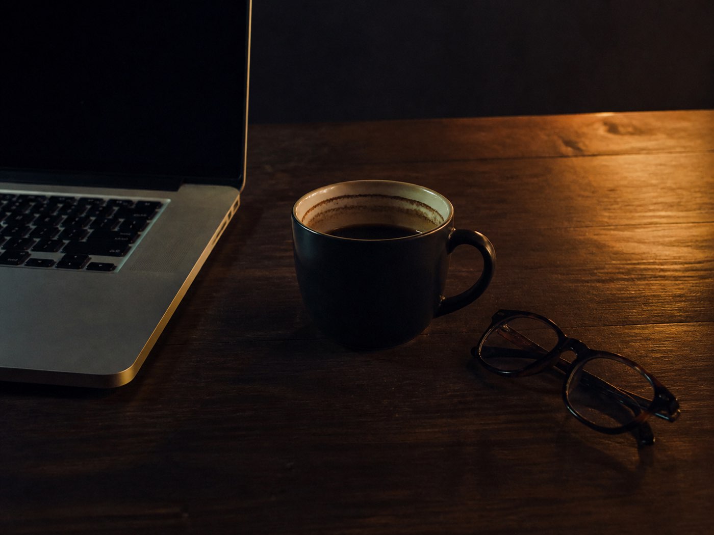A desk at the end of a long working day, lamp on, screen glow