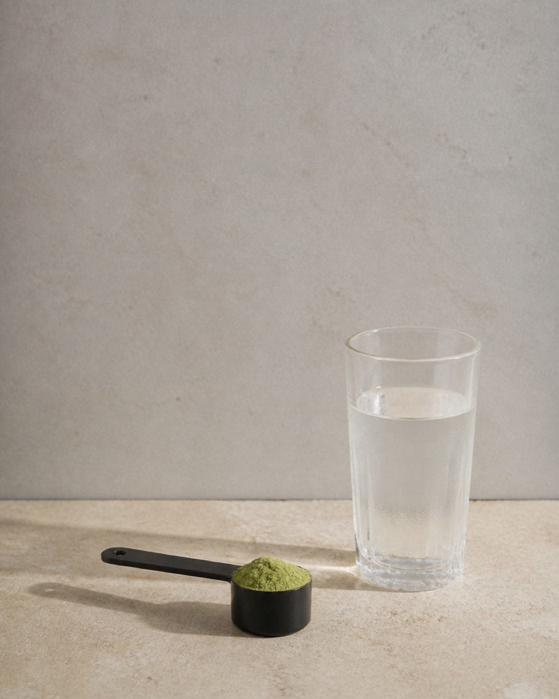 A single scoop of Daily Greens resting on a stone counter beside a glass of cold water