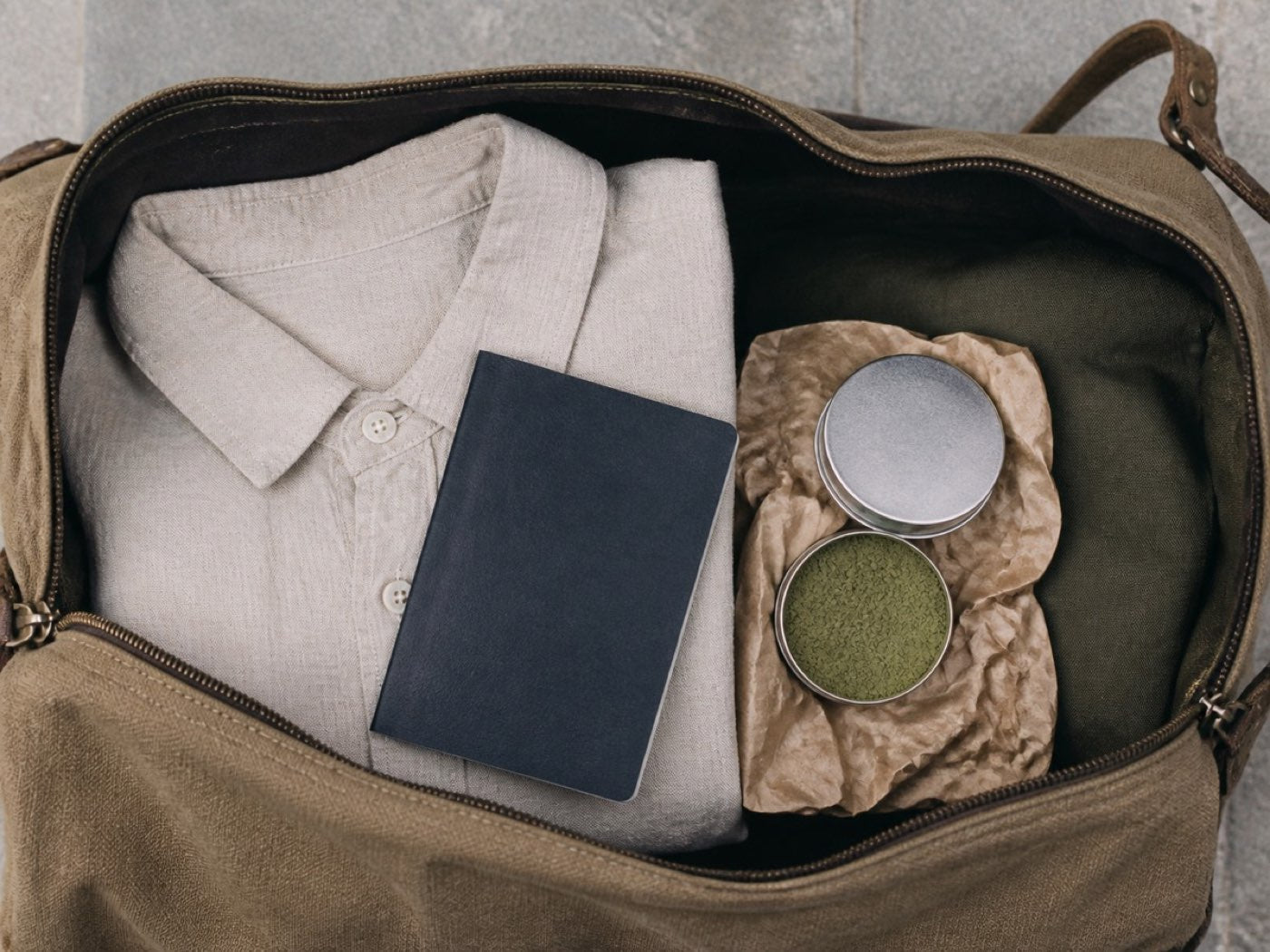 A small steel tin of pre-portioned powder packed beside a passport and a folded shirt