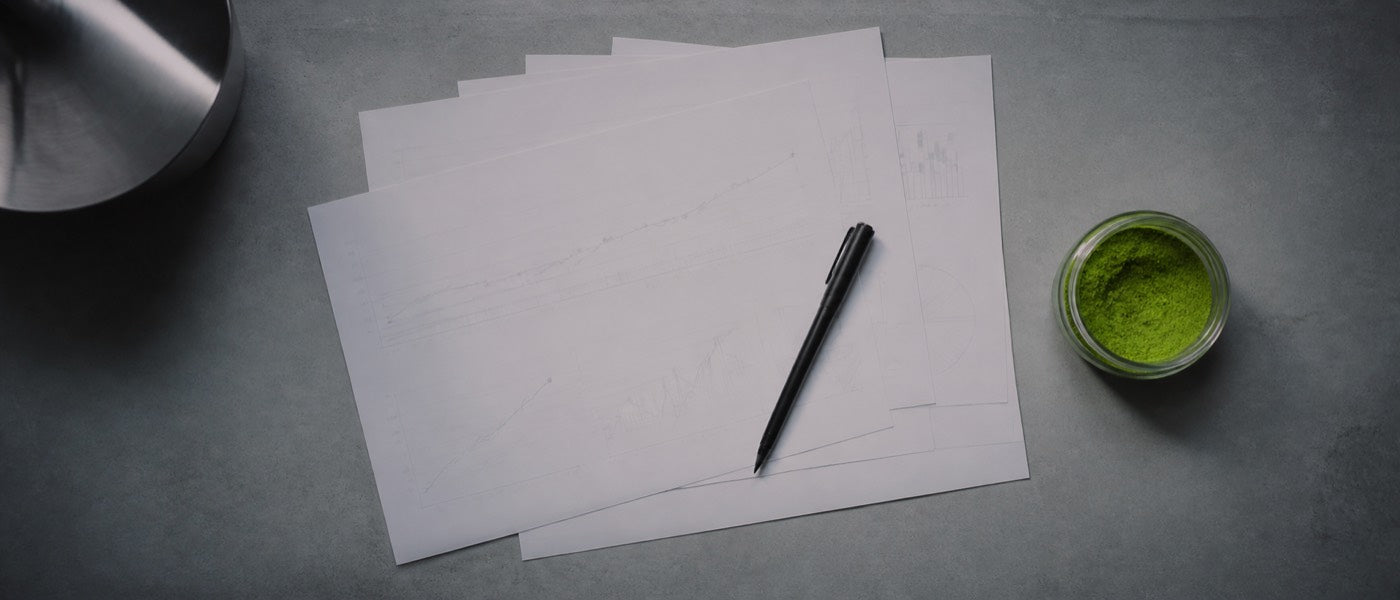 Fanned charts and a pen beside a jar of green powder