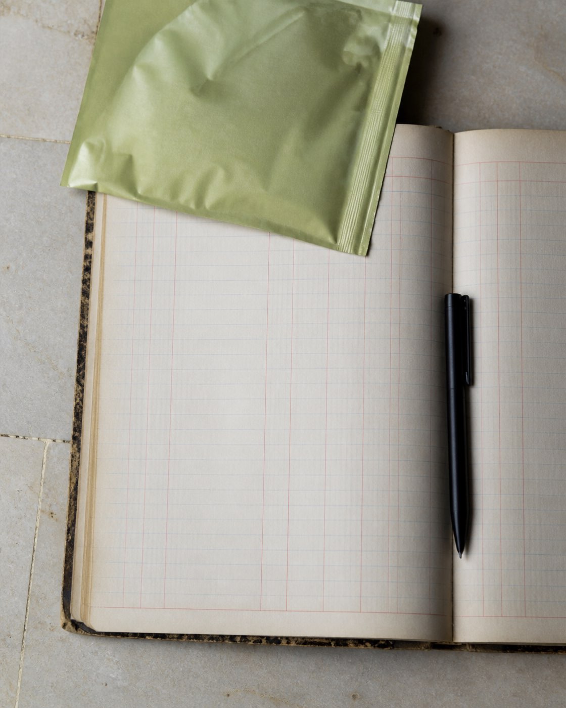 A single pouch on a plain desk beside an open ledger notebook and a pen