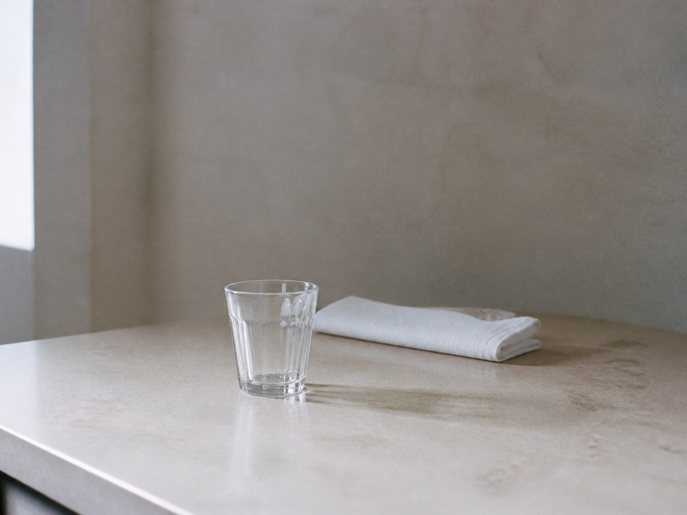 An empty kitchen counter in morning light with a single glass on it