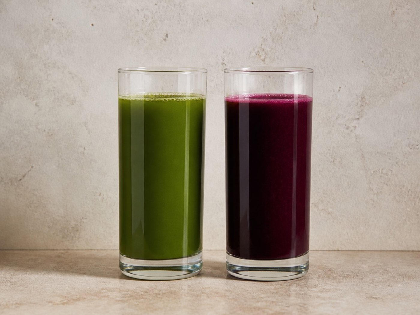 Two glasses side by side, one green and one deep purple, on a plain surface