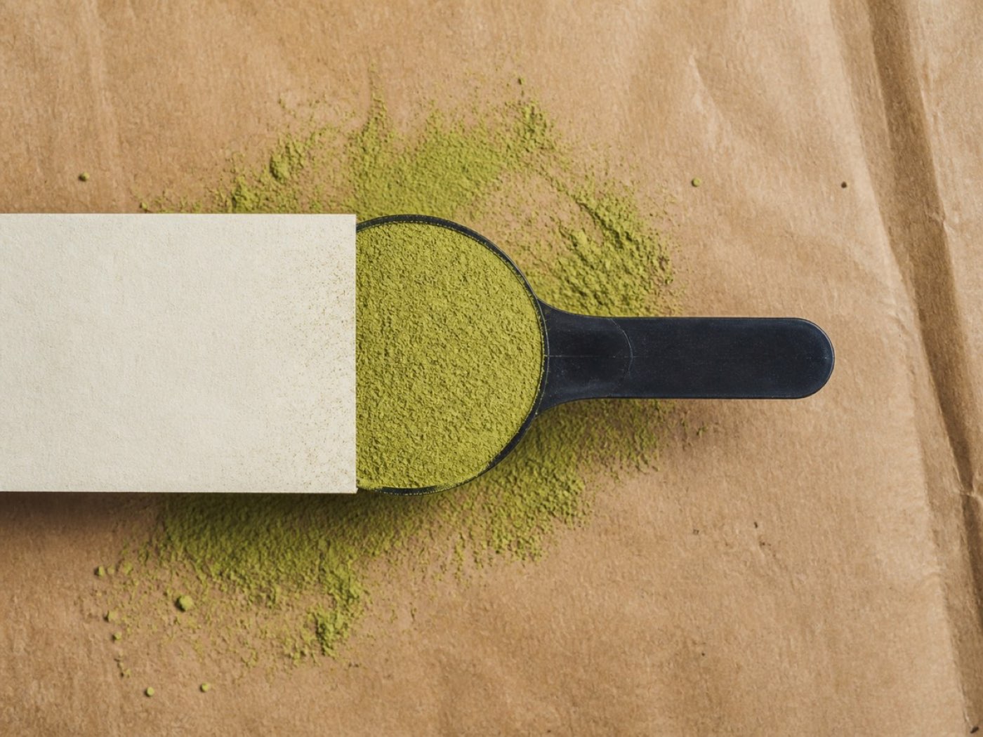 One scoop of green powder being levelled off against the rim of a black scoop