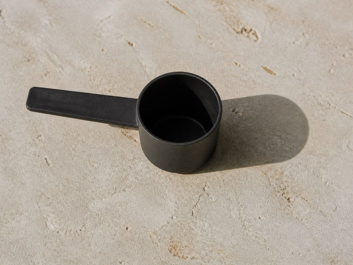 A matte black measuring scoop resting on a stone surface